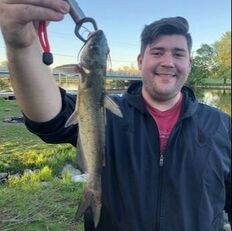 Picture of Tyler Butts, holding up a fish on a stringer in front of a small waterbody